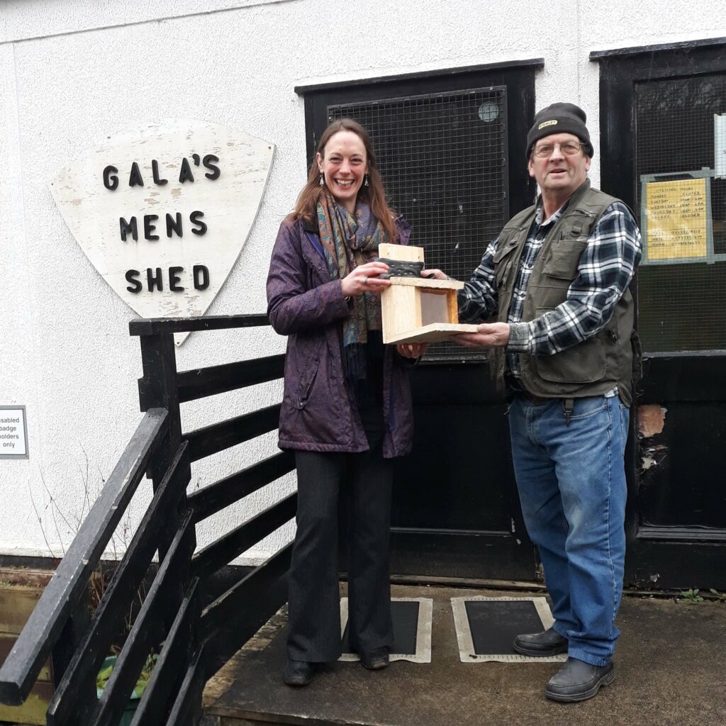 Man presenting feeder box to Alexa outside Men's Shed