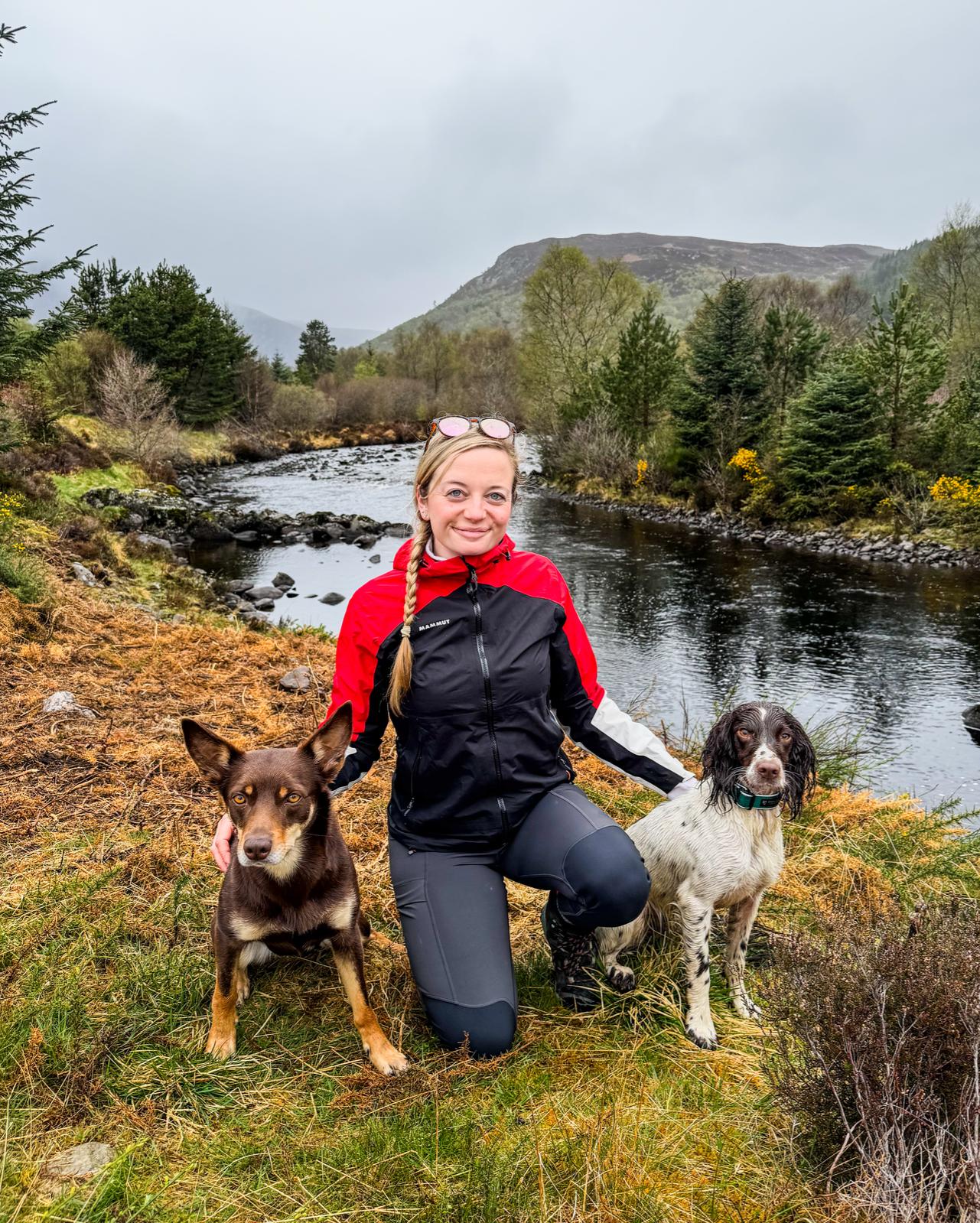 Libby posing with Sika and Tarka next to a river.